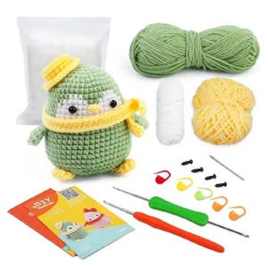 May include: A crochet penguin kit with green, yellow, and white yarn, a crochet hook, and a DIY instruction booklet. The finished penguin has a green body, yellow hat and scarf, and white accents. Includes stuffing, stitch markers, and safety eyes.