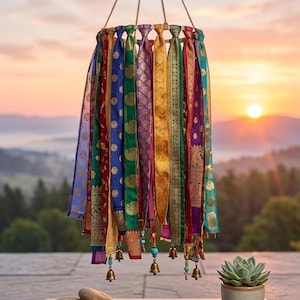 May include: A hanging mobile featuring a circular frame adorned with numerous vertical strips of colorful patterned fabric in shades of blue, green, gold, purple, and red, accented with small metallic bells and turquoise beads at the bottom ends.