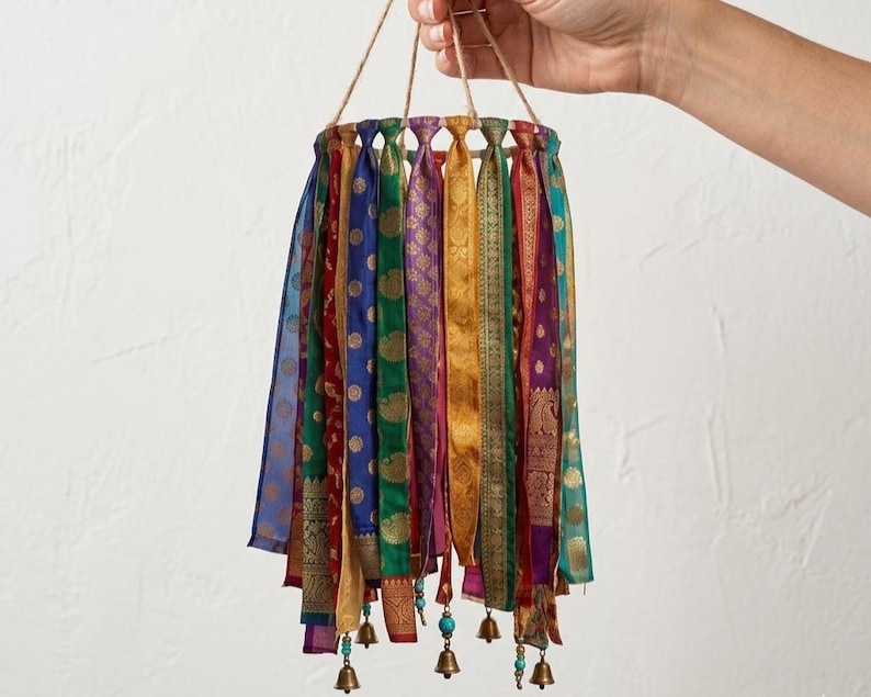 May include: A circular hanging mobile featuring numerous vertical fabric ribbons in vibrant shades of blue, green, red, gold, and purple, each adorned with intricate patterns. Small metallic bells and turquoise beads hang from the bottom edges.