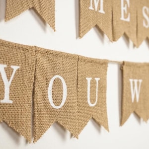 May include: A banner made of burlap material with white lettering spelling out "YOU WANT MESSAGE". The banner is strung on a thin twine and is hanging against a white background. The banner flags have a pointed bottom.