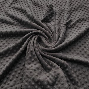 May include: A dark gray minky fabric featuring a raised, textured dot pattern across the entire surface. The material is gathered in a central spiral, showcasing the soft, plush quality and the consistent arrangement of the small, round bumps.