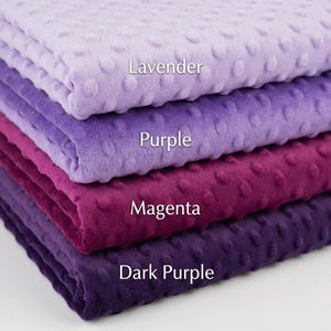 May include: A stack of four plush fabrics in shades of purple, from light lavender to deep dark purple. Each fabric has a textured, dotted surface. The names of the colors are labeled on each fabric: Lavender, Purple, Magenta, and Dark Purple.