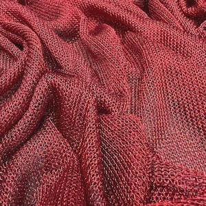 Könnte beinhalten: Nahaufnahme eines tiefroten, gewebten Stoffes mit einem netzartigen Muster. Das Material ist drapiert und gefaltet, wodurch Schatten und Lichtreflexe entstehen, die die Textur hervorheben. Der Stoff scheint leicht zu sein und kann für Kleidung oder Dekorationszwecke verwendet werden.
