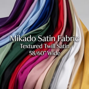 May include: A collection of Mikado satin fabric in various colors, including deep purple, blue, green, red, and gold. The fabric is textured twill satin and is 58/60 inches wide. The image displays the fabric in flowing folds.