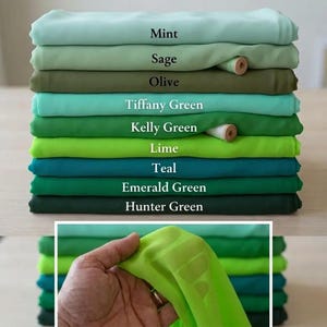 May include: A stack of folded fabric in various shades of green, labeled Mint, Sage, Olive, Tiffany Green, Kelly Green, Lime, Teal, Emerald Green, and Hunter Green. A piece of bright lime fabric is held up in the foreground to show texture.
