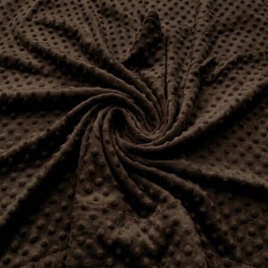 May include: A dark brown fabric featuring a raised dimpled texture across the entire surface. The material is gathered in a central swirl, highlighting the consistent pattern of small, rounded bumps that create a tactile, three-dimensional effect.