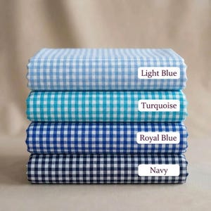 May include: A stack of four folded fabric pieces in light blue, turquoise, royal blue, and navy. Each fabric has a gingham pattern. The colors are labeled with white rectangular tags: "Light Blue", "Turquoise", "Royal Blue", and "Navy".