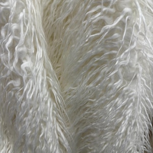 May include: Close-up of a white, shaggy faux fur fabric. The fabric has long, wavy strands that create a textured, fluffy appearance. The colour is a bright, clean white, and the material appears soft and luxurious.