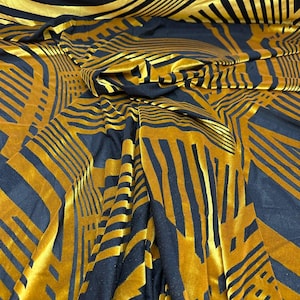 May include: Close-up of a folded fabric with a geometric pattern. The fabric is a deep navy blue with a gold, velvet-like design. The pattern consists of lines and shapes, creating a modern, abstract look. The fabric appears soft and luxurious.