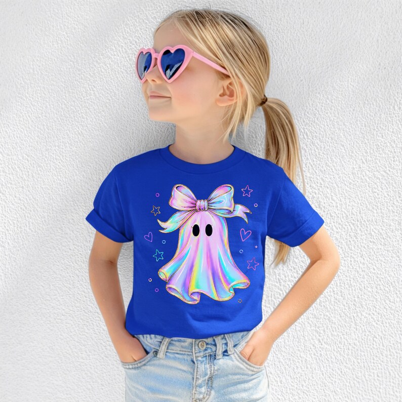 Puede incluir: Una camiseta de manga corta azul real con un gr&aacute;fico central de un fantasma de estilo hologr&aacute;fico que lleva un lazo grande, rodeado de peque&ntilde;as estrellas y corazones delineados. El fantasma tiene dos ojos ovalados negros y un acabado iridiscente.
