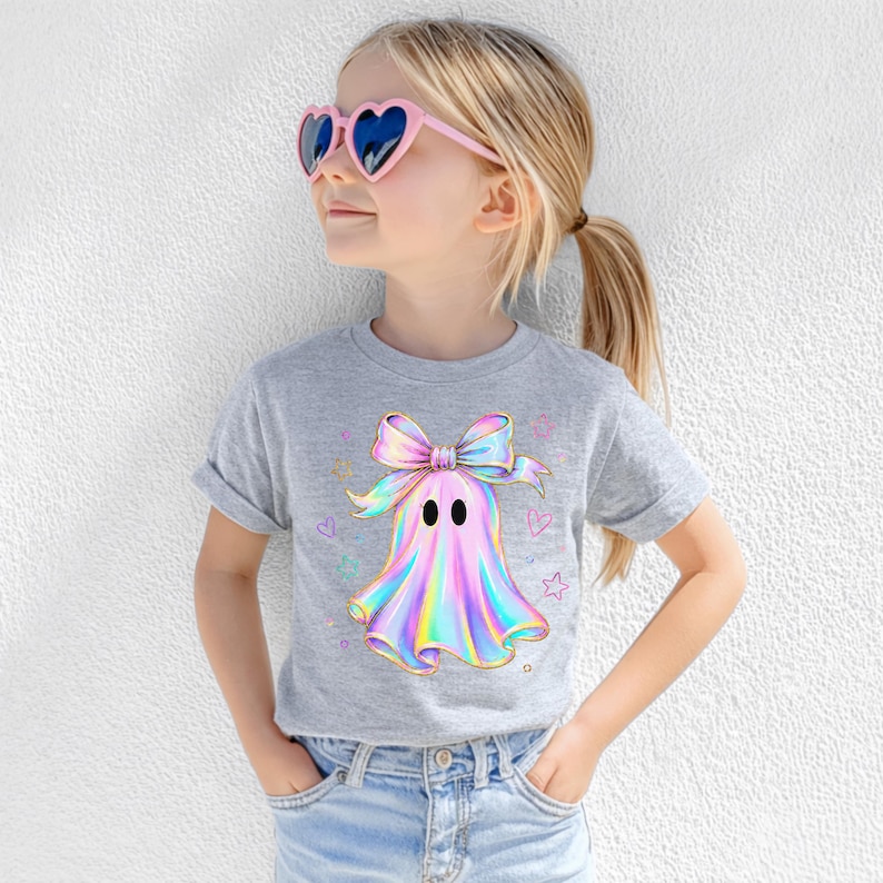 Puede incluir: Una camiseta gris jaspeado de manga corta con un gr&aacute;fico central de un fantasma que lleva un gran lazo iridiscente. El dise&ntilde;o del fantasma muestra una paleta de colores hologr&aacute;ficos en rosa, azul y amarillo, rodeado de peque&ntilde;as estrellas y corazones.