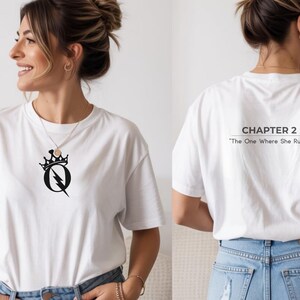 May include: White t-shirt with a black graphic on the front featuring a crown, lightning bolt, and the letter "Q". The back of the shirt displays the text "CHAPTER 2" and "The One Where She Rules".