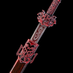 Puede incluir: Una espada con una hoja metálica que presenta un diseño de dragón grabado. La empuñadura y la vaina están adornadas con intrincados patrones de filigrana de metal rojo en relieve. El mango es texturizado y la guarda muestra un diseño rojo.