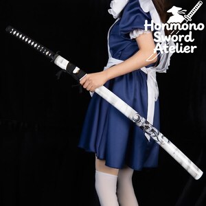 May include: A katana with a black handle and a white and gray scabbard. The scabbard features a black and white graphic design. The blade is black with a silver edge. The text "Honmono Sword Atelier" is visible in the image.