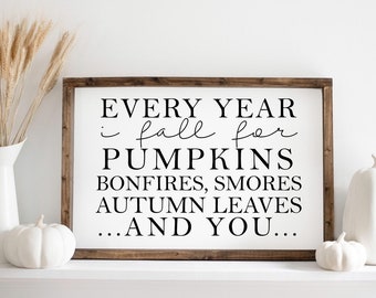 May include: A white wooden sign with black text that reads "EVERY YEAR i fall for PUMPKINS BONFIRES, SMORES AUTUMN LEAVES ...AND YOU..."