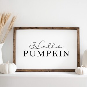 May include: A white wooden sign with the text "Hello Pumpkin" in black lettering. The sign is sitting on a white shelf with two white pumpkins.