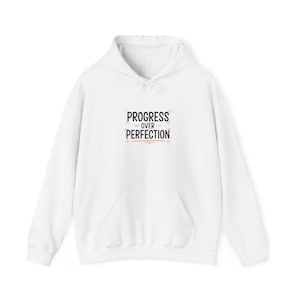 May include: White hoodie with a front pocket and drawstring hood. The front of the hoodie features the text "PROGRESS OVER PERFECTION" in a black and orange design.