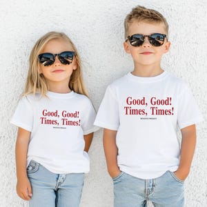 May include: Two white short-sleeve t-shirts featuring the red text "Good, Good! Times, Times!" and "BOLOVO PROUCT" printed on the chest. The shirts are paired with light blue denim jeans and black sunglasses, creating a coordinated casual look.