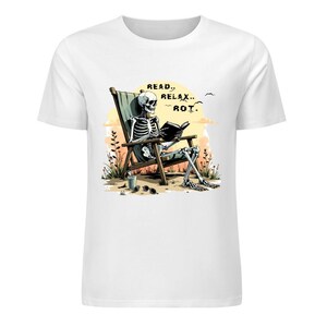 White t-shirt featuring a skeleton relaxing in a beach chair reading a book with the text Read Relax Rot in a warm sunset illustrated design