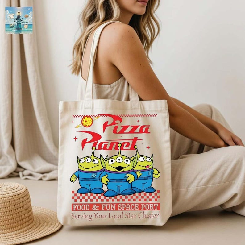 A woman is sitting on the floor with a tote bag featuring a design of three alien characters from the Pixar movie "Pizza Planet".