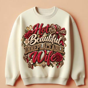 May include: A cream-colored crewneck sweatshirt featuring a central graphic design with the text Hot Beautiful IRREPLACEABLE Wife. The design includes red roses, white flowers, gold hearts, and a leopard print bow, all arranged in a decorative cluster.