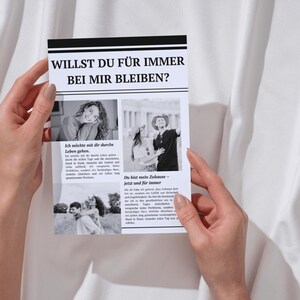 Pode incluir: Um cart&atilde;o impresso em preto e branco segurado por m&atilde;os, com o texto "WILLST DU F&Uuml;R IMMER BEI MIR BLEIBEN?" e imagens. O cart&atilde;o tem uma borda preta e est&aacute; sobre um fundo branco.