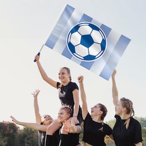 May include: A group of women celebrate, holding a soccer flag with a blue and white soccer ball design. The flag has blue and white stripes. The women are wearing black shirts and are cheering.