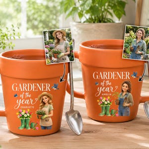 May include: Two orange ceramic mugs shaped like flower pots, each featuring a handle and a spoon. The mugs display the text "GARDENER of the year" with illustrations of a person, flowers, and boots. Each mug includes a small photo insert.