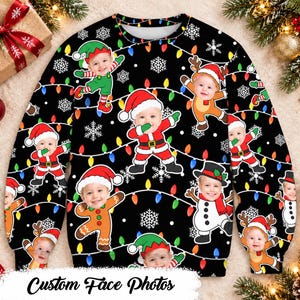 May include: A black long-sleeved sweatshirt featuring a repeating pattern of colourful Christmas lights, white snowflakes, and cartoon characters with a custom face photo. The characters include elves, reindeer, Santa Claus, and a snowman.