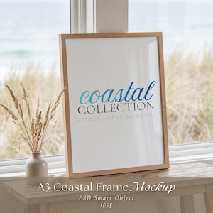May include: A vertical A3 wooden picture frame containing a white insert with the blue text coastal and the black text COLLECTION and LITTLE LAYNE MOCKUPS. The frame is positioned next to a small ceramic vase holding dried wheat stalks.