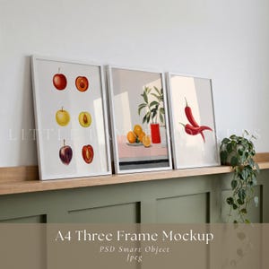 Könnte beinhalten: Drei gerahmte Kunstdrucke mit Aquarellillustrationen. Ein Druck zeigt Äpfel und Pflaumen, ein anderer Orangen und eine Vase, der dritte rote Chilischoten. Die Rahmen sind weiß, und der Gesamteindruck ist minimalistisch.