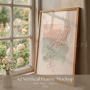 以下が含まれることがあります： バラに手を伸ばす手のミニマリストな線画が描かれた、額入りのアートプリント。ピーチとティールの水彩ウォッシュが特徴です。フレームは明るい色の木製です。下部のテキストは「A2 Vertical Frame Mockup」と書かれています。