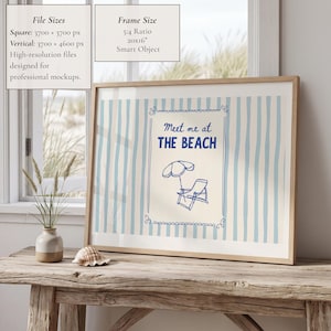 May include: A framed print with a beach theme. The artwork features blue and white vertical stripes, with a central design that reads "Meet me at THE BEACH" and includes a beach umbrella and chair. The frame is a light wood colour.