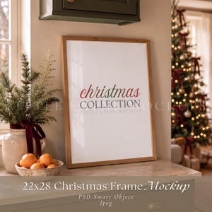 Può includere: Una cornice portafoto verticale in legno contenente un inserto bianco con il testo rosso e grigio "christmas COLLECTION". La cornice è posizionata su una superficie accanto a un vaso in ceramica con rami di pino e una ciotola di arance.