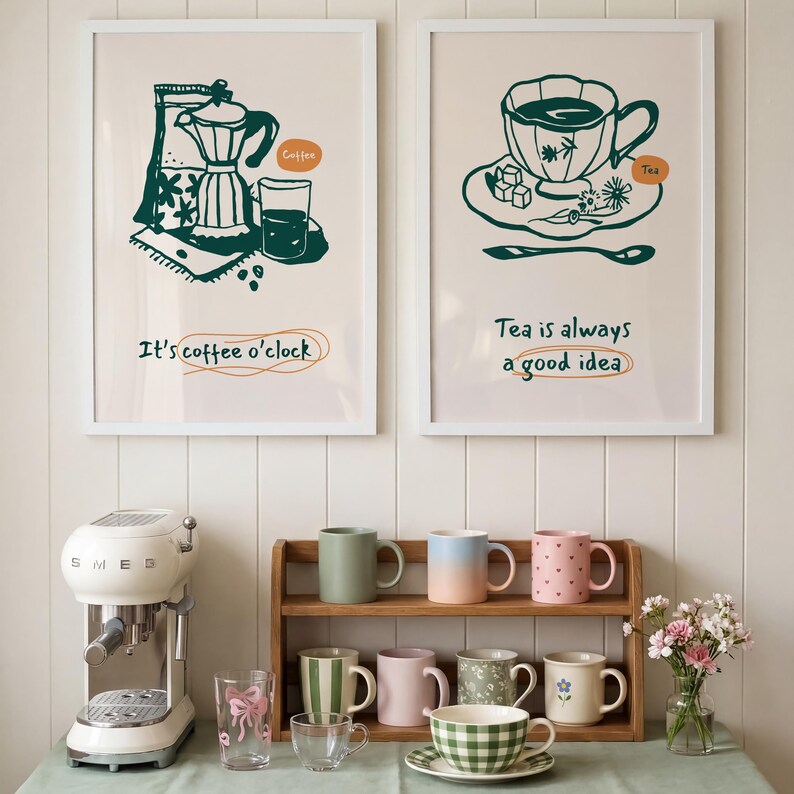 May include: Two framed prints with coffee and tea illustrations hang above a display of mugs and a coffee machine. The prints read "It's coffee o'clock" and "Tea is always a good idea." Various mugs in different colors and patterns are arranged on a wooden shelf.
