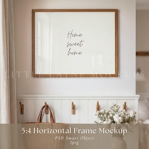May include: A framed mockup with the words "Home sweet home" in a script font. The frame is a warm brown color and is hanging on a white wall. Below the frame is a white panel with wooden hooks and a woven basket.