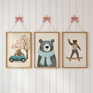 May include: Three framed art prints with cartoon bears. One shows a bear driving a blue car, another a bear with a blue scarf, and the last a bear on a skateboard. Each print is hung with a string and a red and white bow.