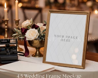 May include: A vertical gold picture frame with a white insert featuring a diamond grid pattern and the text YOUR IMAGE HERE. The frame is displayed next to a black instant camera, a brass bowl filled with white roses and dark red ribbons.