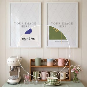 May include: A display of mugs, cups, and a teacup set on a wooden shelf and table. The mugs are in various colors, including green, pink, and blue. A white espresso machine is on the left. Two framed art prints hang on the wall.