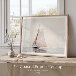 May include: A framed watercolour print of a sailboat on the sea. The artwork is in a light wood frame and rests on a rustic wooden table. A small vase with tall grass and a seashell are also on the table. The text "5:4 Coastal Frame Mockup" is at the bottom.