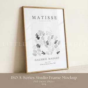 May include: A vertical rectangular gold-toned frame containing a white poster with black text reading MATISSE PAPIER DÉCOUPÉS, GALERIE MAEGHT, Paris 1934, 13 Rue de Teheran, Paris VIII, and a central graphic of abstract dark gray leaf-like shapes.