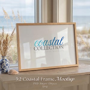 Op de afbeelding: Een rechthoekige houten fotolijst met een witte inleg met de blauwe tekst "coastal" en de grijze tekst "COLLECTION" en "LITTLE LAYNE MOCKUPS". De lijst staat op een houten oppervlak naast een blauw-witte vaas met gedroogd gras.