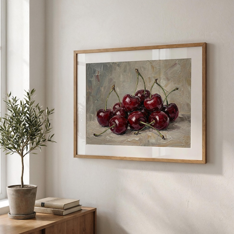 Op de afbeelding: Een ingelijst schilderij van een tros rijpe, donkerrode kersen met groene steeltjes. Het kunstwerk wordt gepresenteerd in een lichtbruine houten lijst, hangend aan een witte muur. Het schilderij heeft een neutrale achtergrond en wordt verlicht door natuurlijk licht.
