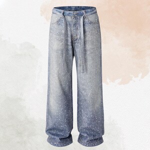May include: Light blue denim jeans with a wide leg design. The jeans are embellished with small, scattered white accents and feature a decorative chain belt. The waistline and belt loops are also detailed with embellishments.