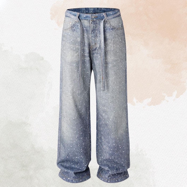 May include: Light blue denim jeans with a wide leg design. The jeans are embellished with small, scattered white accents and feature a decorative chain belt. The waistline and belt loops are also detailed with embellishments.