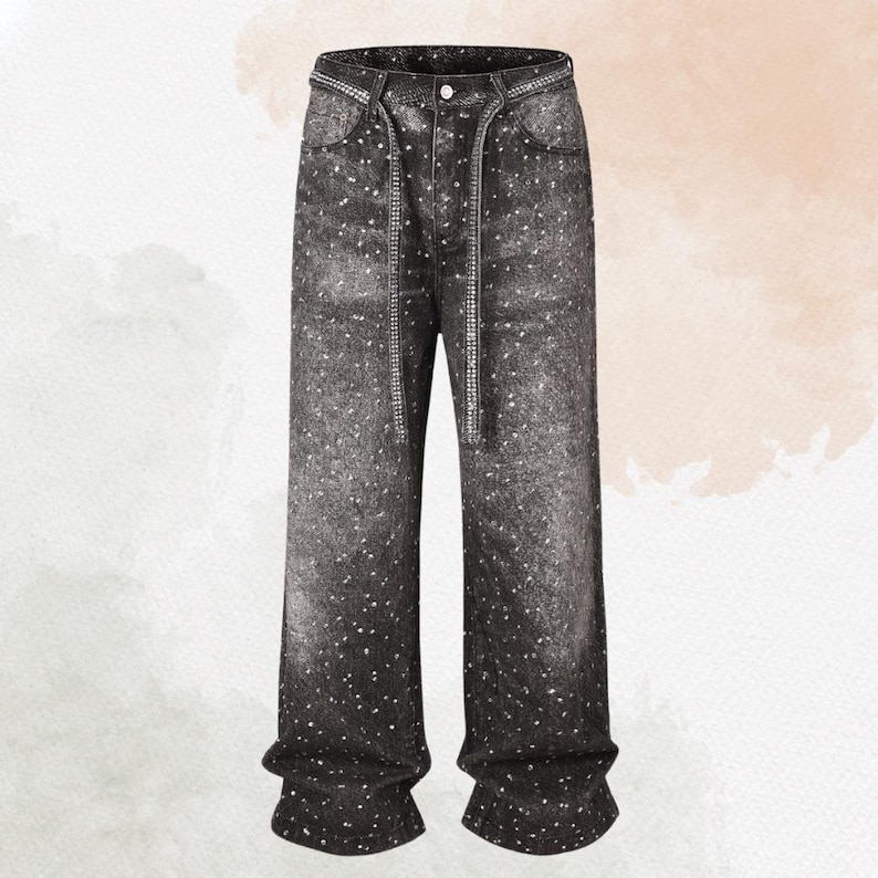 May include: Black denim jeans with a white speckled pattern. The jeans have a drawstring waist and a button closure. The pockets and waistline are embellished with a silver-colored trim. The jeans have a wide-leg fit.