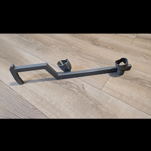 May include: A grey, 3D-printed object with a distinctive shape. It has a handle, a central angled section, and two cup-like holders. The design suggests it may be a specialised tool or accessory, possibly for a specific purpose.