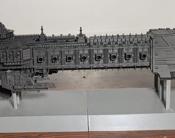 May include: A matte black plastic model of a large spaceship featuring a long, rectangular hull with multiple side-mounted weapon ports, a detailed bridge section, and a wide, flared rear engine assembly, all mounted on a light gray display stand.