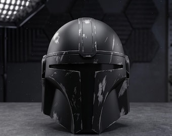 May include: A matte black helmet featuring a T-shaped visor and a weathered, distressed finish with silver-toned scuffs and scratches across the surface. The helmet has a structured, rounded dome and angular cheek plates, presenting a worn appearance.