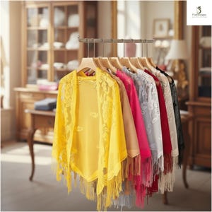 May include: A display of colorful shawls hanging on wooden hangers. The shawls are in various colors, including yellow, pink, red, and gray. Each shawl has a delicate lace design and fringe.